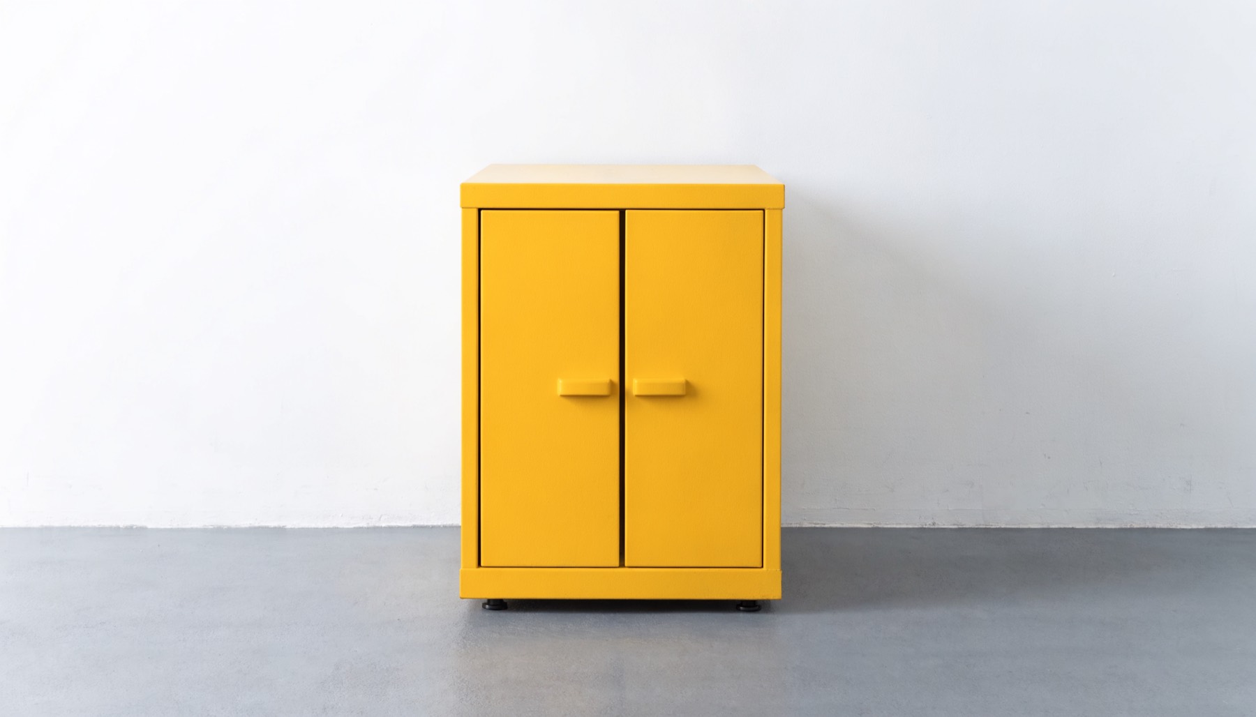 A closed yellow metal safety storage cabinet against a white wall